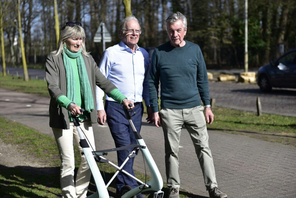 Three people walking with a walker outdoors