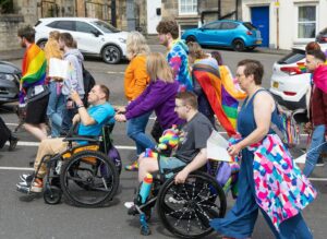 Diverse group, including wheelchair users, at a vibrant pride parade.